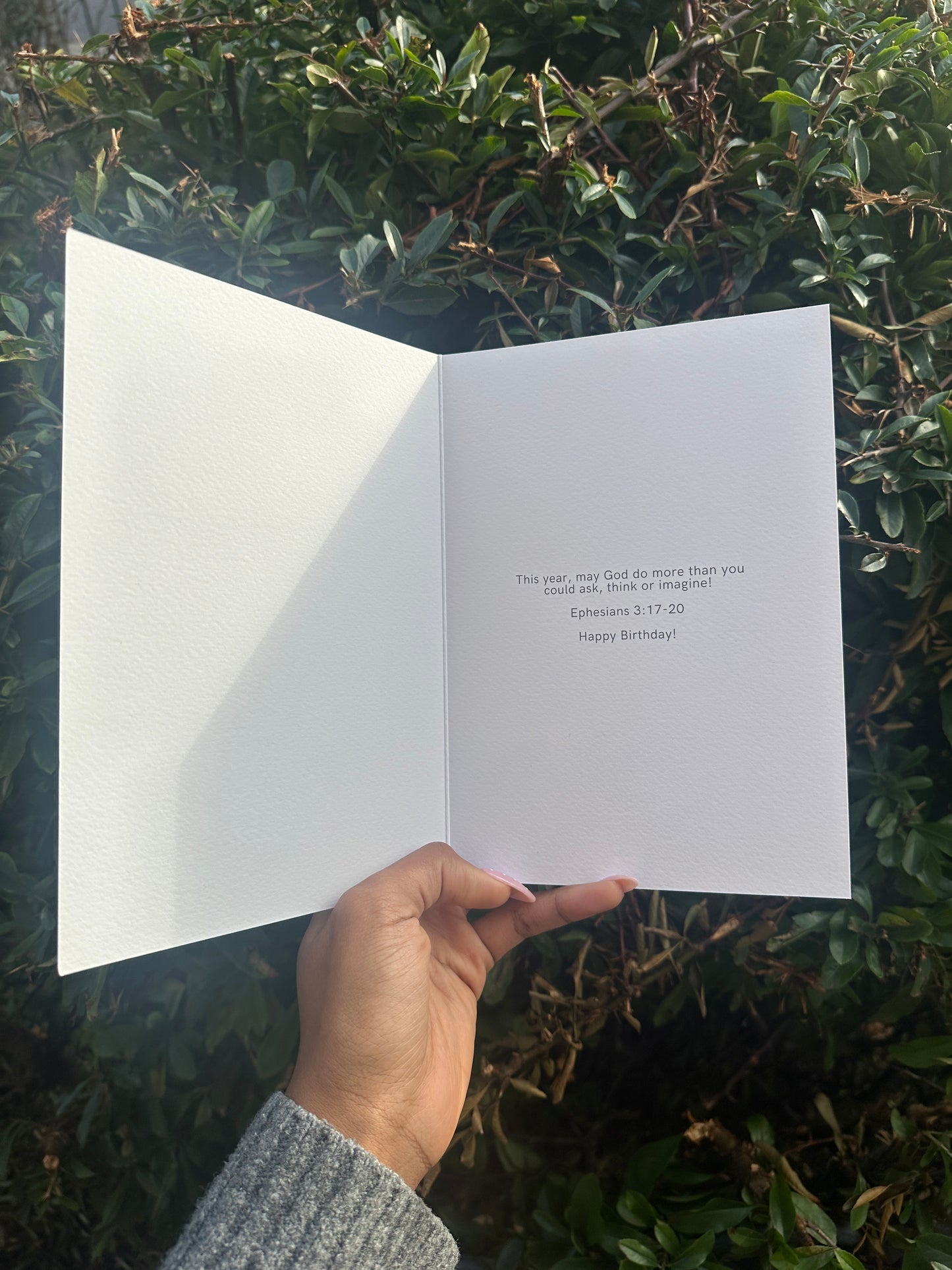 Hand holding a white card with text against a green leafy background