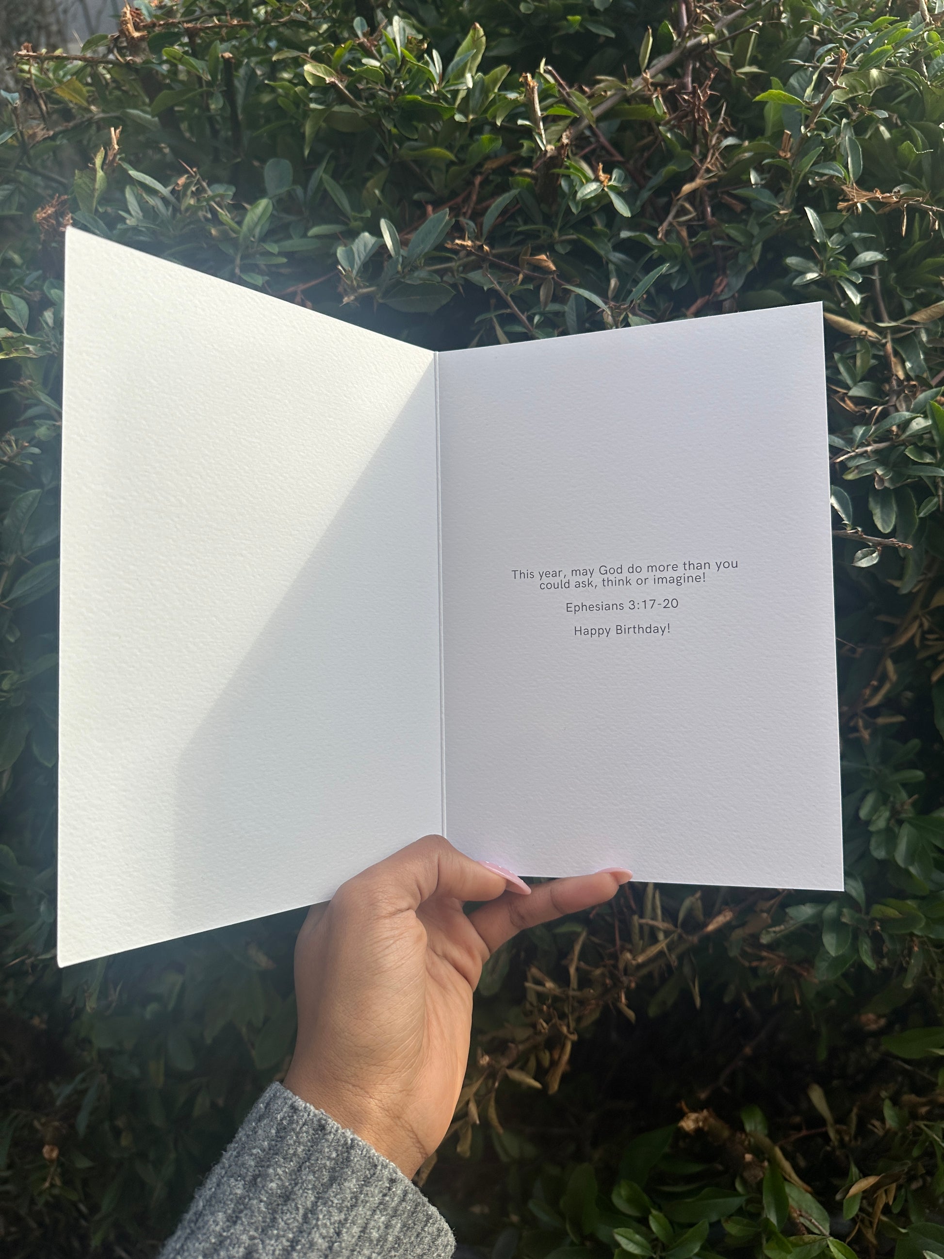 Hand holding a white card with text against a green leafy background